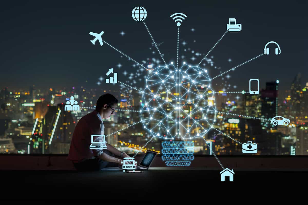 Polygonal brain shape of an artificial intelligence with various icon of smart city Internet of Things Technology over Asian businessman sitting and using the laptop over the cityscape background